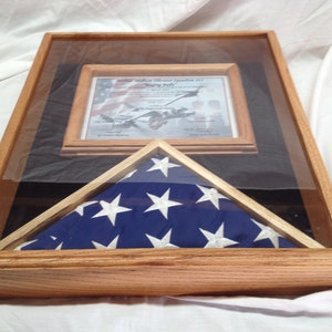 May include: A wooden display case with a framed certificate and a folded American flag. The flag is blue with white stars and red and white stripes. The certificate is in a wooden frame and has text and an image.