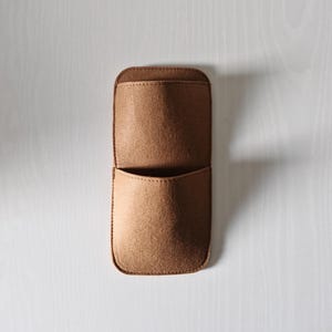 May include: A brown felt organizer with two pockets, stitched along the edges. The top pocket is larger than the bottom one. The organizer is designed to hold small items and is shown against a white background.