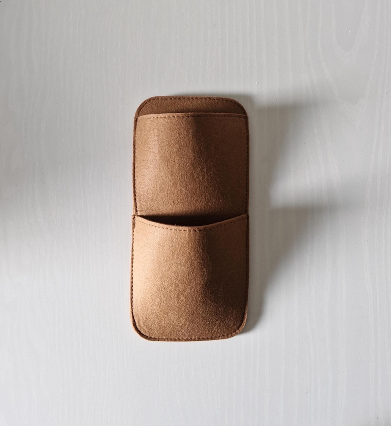 May include: A brown felt organizer with two pockets, stitched along the edges. The top pocket is larger than the bottom one. The organizer is designed to hold small items and is shown against a white background.
