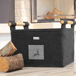 May include: A grey felt firewood basket with wooden handles. The basket has a deer silhouette on the front and the text "Stich-haltig" on a white tag.