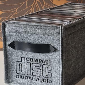 May include: A gray felt CD storage box with a black leather handle and the text "COMPACT DISC DIGITAL AUDIO" printed on the front.