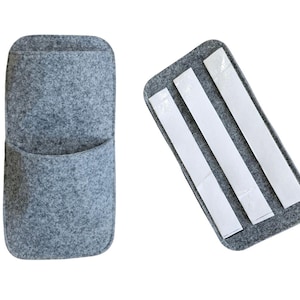 May include: Two gray felt organizers. One is a pocket-style wall organizer with a rounded top and a curved pocket. The other is a rectangular felt piece with three adhesive strips on the back for mounting.