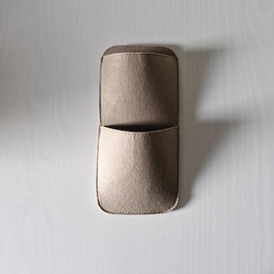 May include: A beige felt wall organizer with two pockets. The top pocket is open, and the bottom pocket is slightly smaller. The organizer is rectangular with rounded corners and is designed to be mounted on a wall.