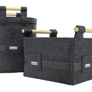 May include: Two grey felt storage baskets with wooden handles. The larger basket is cylindrical and the smaller basket is rectangular. Both baskets have a black leather trim and a small label with the text "Black Bunny" on them.