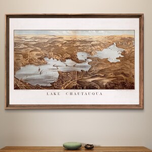 Puede incluir: Un mapa vintage enmarcado del lago Chautauqua, Nueva York, con un marco de madera marr&oacute;n y un passe-partout blanco. El mapa muestra el lago y el &aacute;rea circundante en detalle, con carreteras, edificios y otras caracter&iacute;sticas etiquetadas.