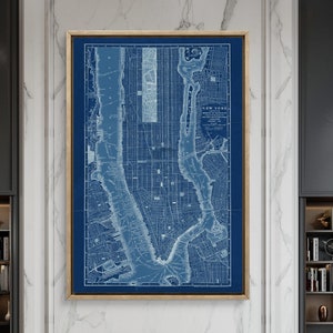 May include: A vintage map of New York City printed in blue and white on a canvas. The map is framed in a gold frame and hangs above a fireplace in a modern living room.