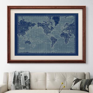 May include: A framed world map print in shades of blue and gray, with a dark brown wooden frame. The map is detailed, showing continents and oceans. The text "THE WORLD" is visible at the bottom. The print hangs above a white sofa and a blue and white coffee table.