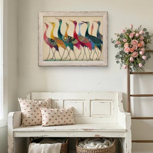 May include: A framed artwork featuring seven colorful birds with long necks and legs. The birds have a variety of colors, including yellow, teal, red, and blue. Below the artwork is a white bench with two heart-patterned pillows and two wicker baskets.