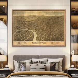 May include: An antique map of Columbus, Ohio, printed in 1875. The map is in a brown frame and shows a bird's-eye view of the city with streets, buildings, and a river.