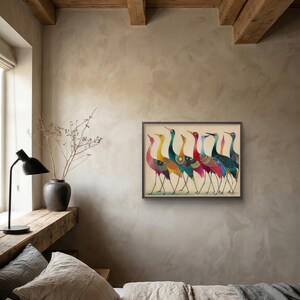 May include: A framed artwork featuring a line of stylized cranes with colorful plumage. The birds have long legs and necks, with a variety of patterns and colors including red, yellow, blue, and green. The artwork is displayed in a room with neutral-toned walls.