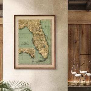 May include: A framed vintage map of Florida, featuring a detailed depiction of the state's geography. The map is in a wooden frame and has a green and beige color scheme. The word "Florida" is printed at the bottom of the map.