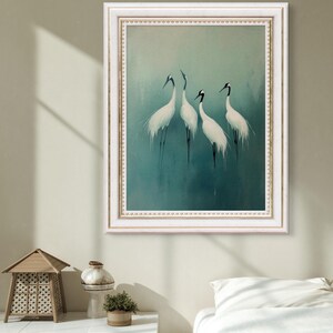 May include: A framed painting of four white cranes with black markings on a teal background. The frame is white with a gold trim.