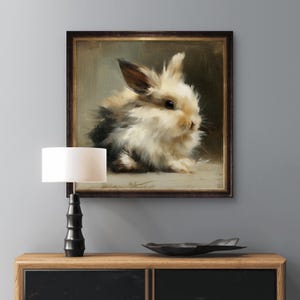 Puede incluir: Pintura enmarcada de un conejo esponjoso con pelaje marr&oacute;n, negro y blanco. La obra de arte est&aacute; en un marco de madera oscura y se exhibe en un mueble de madera. Una l&aacute;mpara negra con una pantalla blanca y un cuenco decorativo negro tambi&eacute;n est&aacute;n en el mueble.