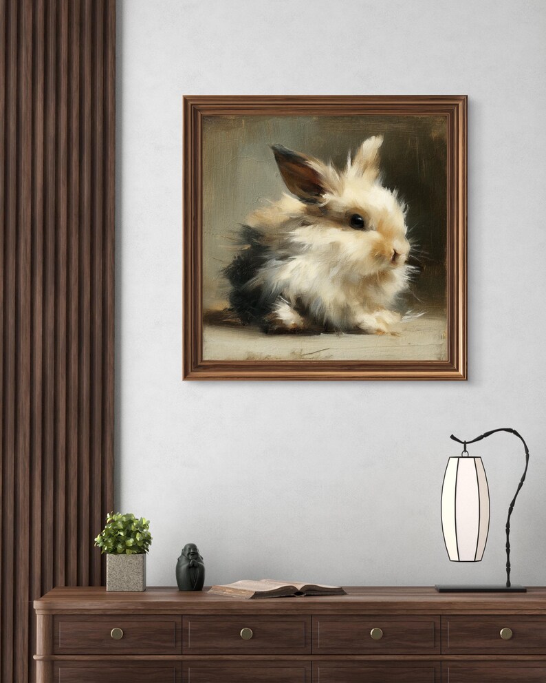 Puede incluir: Una pintura enmarcada de un conejito esponjoso con pelaje negro, blanco y marr&oacute;n claro. La obra de arte est&aacute; en un marco de madera marr&oacute;n y cuelga de una pared blanca. El conejito es el punto focal, con un estilo suave y pict&oacute;rico. El cuadro est&aacute; sobre una c&oacute;moda de madera.