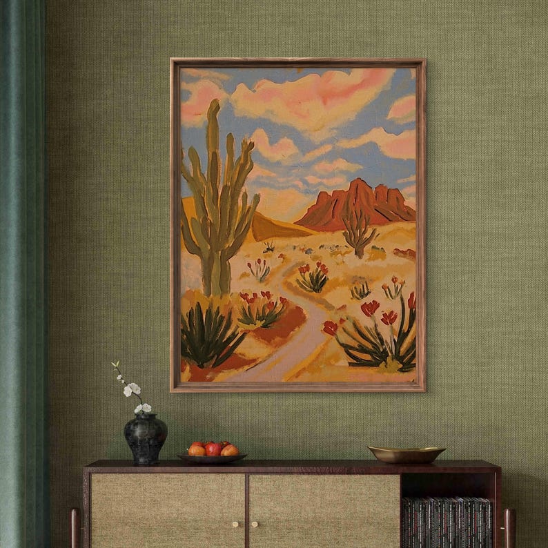 May include: A framed painting of a desert landscape with a tall cactus in the foreground, a winding path leading to a mountain range in the background, and a blue sky with pink clouds.