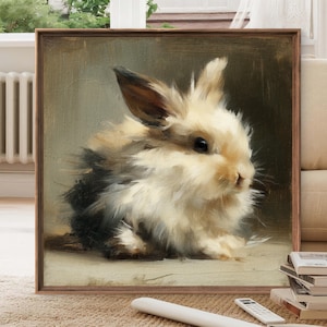 Puede incluir: Pintura enmarcada de un conejo esponjoso. El conejo tiene pelaje color crema con manchas negras y marrones. La obra de arte es de estilo suave e impresionista, con un fondo neutro y un marco de madera.