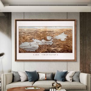 Puede incluir: Una ilustraci&oacute;n de estilo vintage del lago Chautauqua, Nueva York, en un marco de madera marr&oacute;n. La ilustraci&oacute;n muestra el lago y sus alrededores con detalle, con edificios, carreteras y &aacute;rboles.