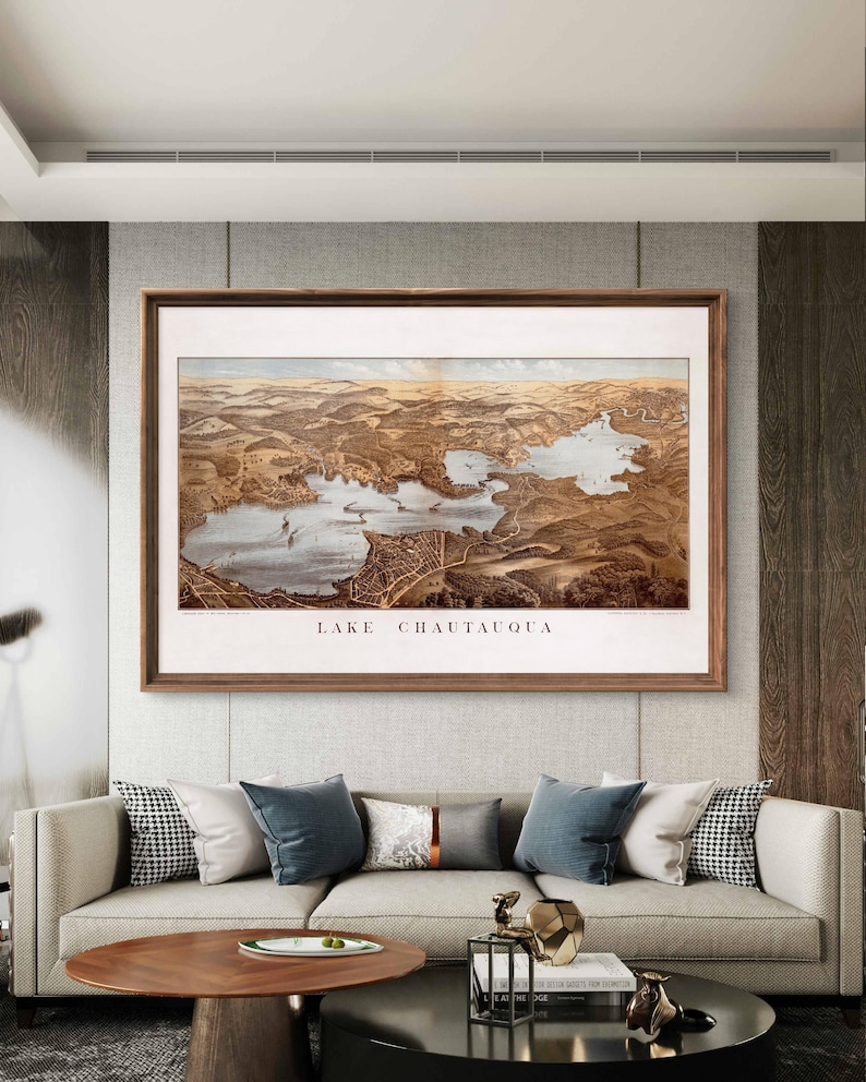 Puede incluir: Una ilustraci&oacute;n de estilo vintage del lago Chautauqua, Nueva York, en un marco de madera marr&oacute;n. La ilustraci&oacute;n muestra el lago y sus alrededores con detalle, con edificios, carreteras y &aacute;rboles.