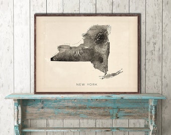 May include: A vintage-style black and white map print of the state of New York with the text "NEW YORK" at the bottom of the print. The print is framed in a brown frame and is hanging on a light wood wall.
