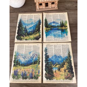 May include: Four printable art prints featuring watercolor paintings of mountain landscapes on a vintage dictionary page background. The prints depict a variety of mountain scenes, including a lake, a forest, and a snow-capped peak.