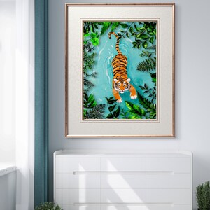 May include: A framed illustration of a tiger swimming in a turquoise blue body of water surrounded by green foliage.