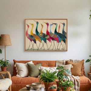 May include: A framed art print featuring a line of colorful birds with long legs and necks. The birds have a variety of colors, including red, yellow, blue, and green. The artwork is displayed in a living room setting with a brown sofa and plants.
