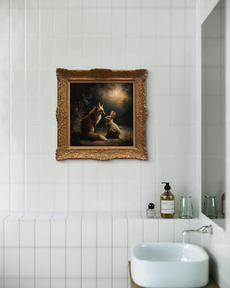 May include: A framed painting depicting a fox and a rabbit in a forest setting. The artwork features warm tones and is set in an ornate gold frame. The painting is mounted on a white tiled wall above a bathroom sink.