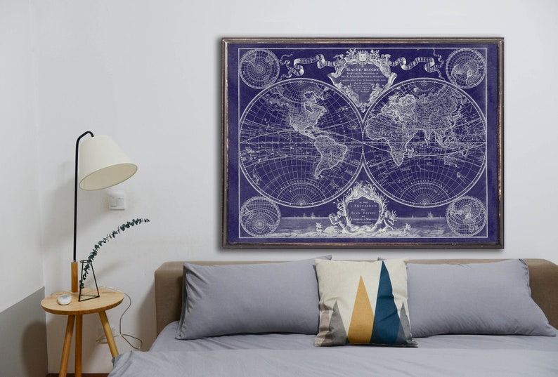May include: A vintage world map print in white on a dark blue background. The map is framed and hanging on a white wall above a gray couch with pillows.