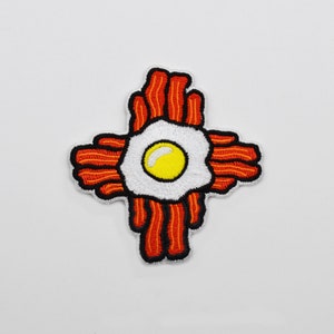 May include: An embroidered patch shaped like the state of New Mexico, with a fried egg in the center and bacon strips surrounding it.