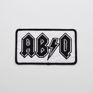 May include: Black and white embroidered patch with the text "AB/Q" in a bold, stylized font.