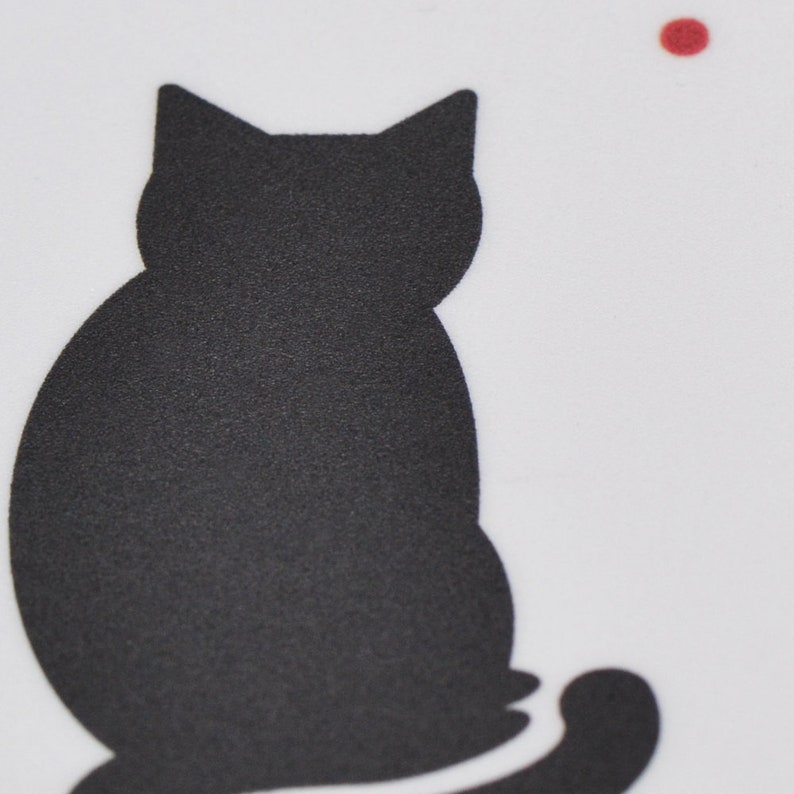 May include: A black silhouette of a cat sitting with its tail curled around its legs. The cat is facing away from the viewer and is looking to the right. There is a small red dot in the top right corner of the image.