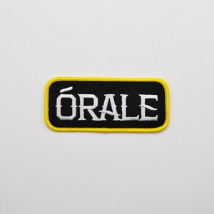May include: Black and yellow embroidered patch with the word "ÓRALE" in white lettering.