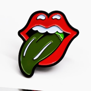 May include: A red and black enamel pin with a tongue sticking out, the tongue is green with white stripes and a green tip.