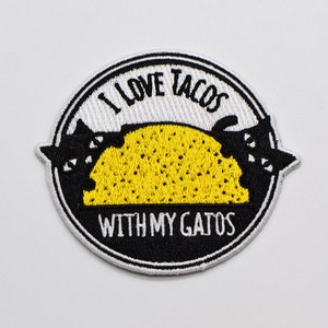 May include: White and black embroidered patch with the text "I love tacos with my gatos" and a yellow taco with two black cats inside.