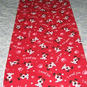 May include: Red fabric with a repeating pattern of cartoon dogs, paw prints, and the text "I woof you" in white. The dogs are white with brown spots and ears. The paw prints are pink.