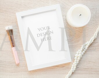 Download Free White frame mockup with candle, pearls, and pink makeup brush on wood stock photo PSD Template