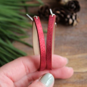 May include: A pair of red glitter hoop earrings. The earrings are made of a thin, flexible material and have a silver hook closure.