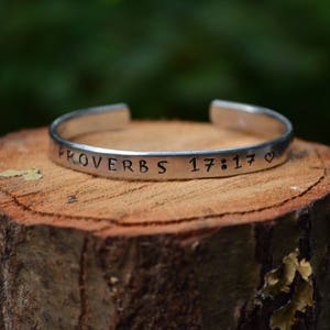 May include: Silver bracelet with the inscription "Proverbs 17:17" and a heart symbol.
