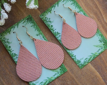 May include: Two pairs of pink teardrop-shaped earrings with gold hooks. The earrings are made of leather with a subtle glitter finish.