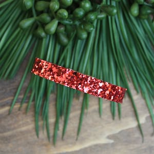May include: A red glitter headband. The headband is made of a thin, flexible material and is covered in red glitter.