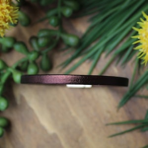 Puede incluir: Un collar de cuero de color morado oscuro con una hebilla plateada.