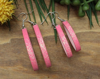 May include: Three pairs of pink glitter dangle earrings with silver hooks. The earrings are different lengths.