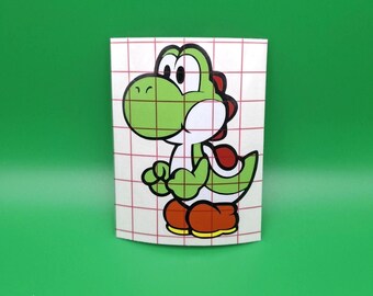 May include: A green and white Yoshi sticker with a red shell and brown shoes. The sticker is on a white background with a red grid pattern, set against a solid green backdrop. The cartoon character is in a friendly pose.