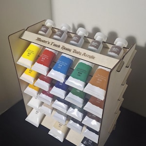 Könnte beinhalten: Ein Holzständer mit Tuben Acrylfarbe in verschiedenen Farben. Die Tuben sind in Reihen angeordnet und mit der Marke "Master's Touch Heavy Body Acrylic" beschriftet. Der Ständer ist aus hellem Holz gefertigt.