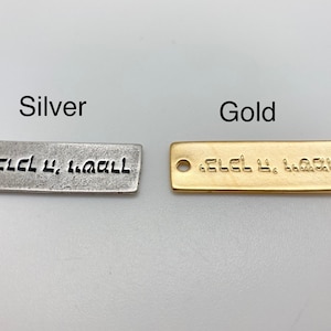 Op de afbeelding: Twee rechthoekige metalen labels, één zilverkleurig en één goudkleurig, met Hebreeuwse tekst. Het zilverkleurige label heeft een gat aan één uiteinde. Het woord "Silver" staat boven het zilverkleurige label en "Gold" staat boven het goudkleurige label.