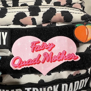 May include: A pink heart-shaped patch with the text "Fairy Godmother" in pink lettering on a black and white leopard print backpack.