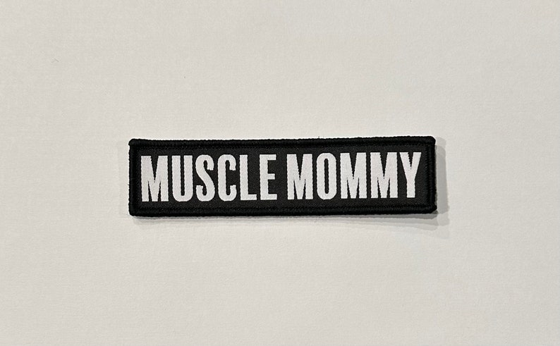 Pu&ograve; includere: Toppa ricamata in bianco e nero con il testo "MUSCLE MOMMY" in lettere bianche.