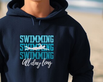 Op de afbeelding: Een marineblauw hoodie met de tekst "Swimming Swimming Swimming All day long" in wit en blauw. Een silhouet van een zwemmer bevindt zich in het midden van de tekst.