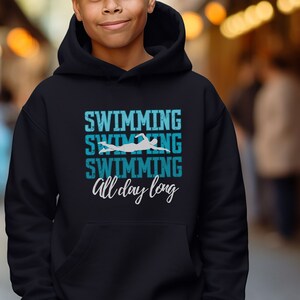 May include: A dark blue hooded sweatshirt with the text "Swimming Swimming Swimming All day long" in white and blue lettering. A silhouette of a swimmer is in the middle of the text.