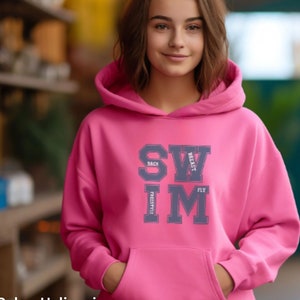 May include: Pink hooded sweatshirt with the word "SWIM" printed on the front in a varsity style font. The letters are outlined in gray and have the words "BACK", "BREAST", "FLY", and "FREESTYLE" printed inside each letter.